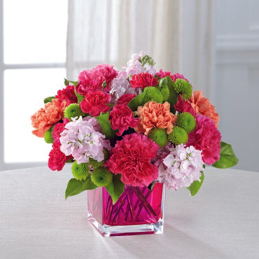 hot pink carnations, pale lavender stock, green button pompons, orange carnations in a clear, pink, glass cube