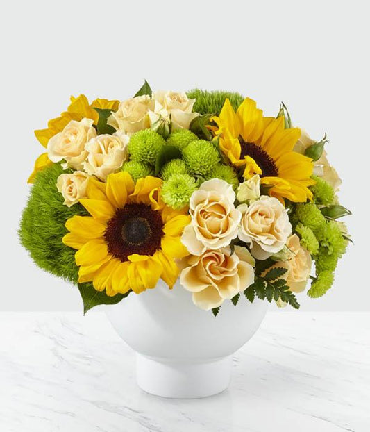 From the bold beauty of bright sunflowers to the sweet delight of peach spray roses. Complete with bursts of green trick dianthus and button pompons, this arrangement is set in a modern white ceramic vase