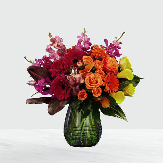 floral arrangement with bright pink mokara orchids, folding into the deep red gerbera daisies, and then melding into the bright orange roses, and vibrant yellow calla lilies