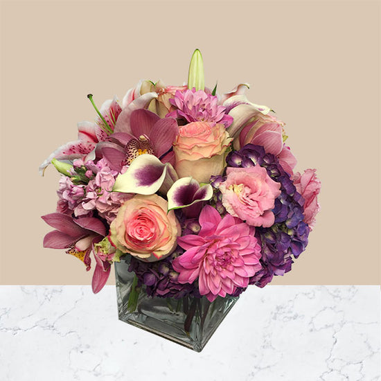 Beautiful mix of spring flowers including roses, hydrangeas, miniature calla lilies, dahlias and lush greens. Presented in a clear glass square