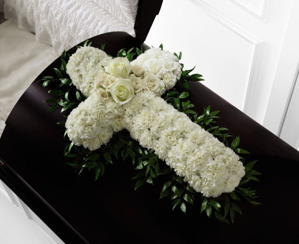  White carnations are arranged in the shape of a cross accented in the middle with white roses and spray roses and along the sides with lush greens to create a lovely casket spray