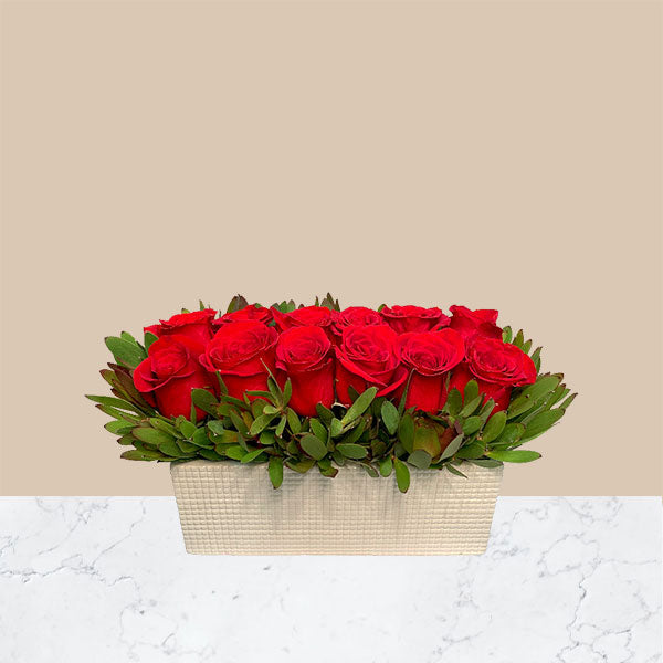 Rows of roses take form in a low compact design. Hand designed in a heart embellished, white ceramic vase. 