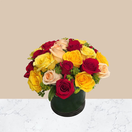 36 mixed colored roses of ellow, peach and red with greens in a clear, short cyclinder vase