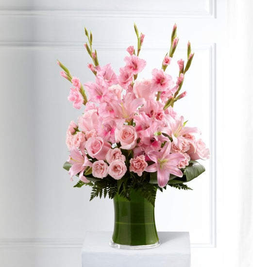 Pink gladiolus, pale pink roses, bi-color pink roses, pink Asiatic lilies and an assortment of lush greens create a sophisticated arrangement seated in a clear glass gathering vase