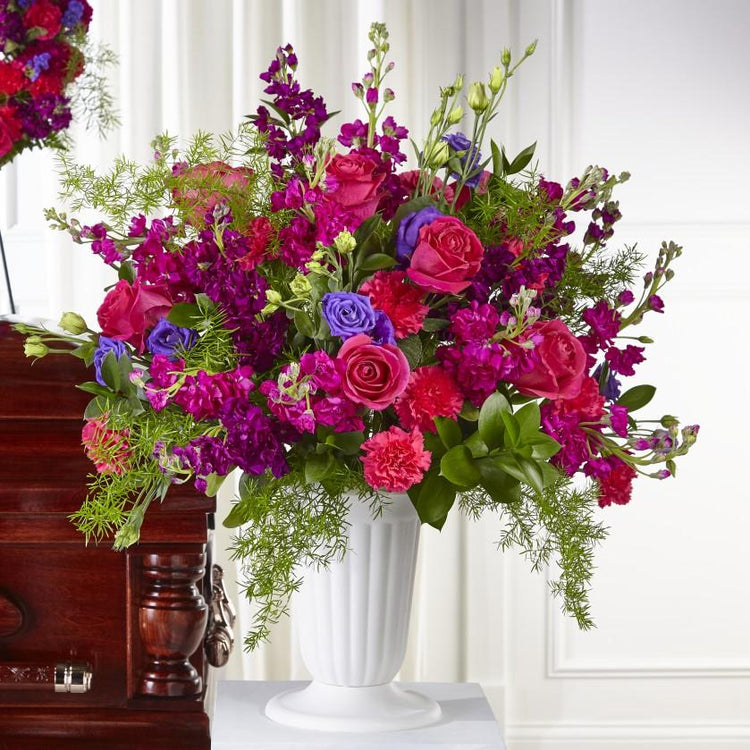 a graceful mixture of purple and hot pink blooms reminds them of your compassion. Each rose, lisianthus, stock and carnation is complemented by a timeless white pedestal urn