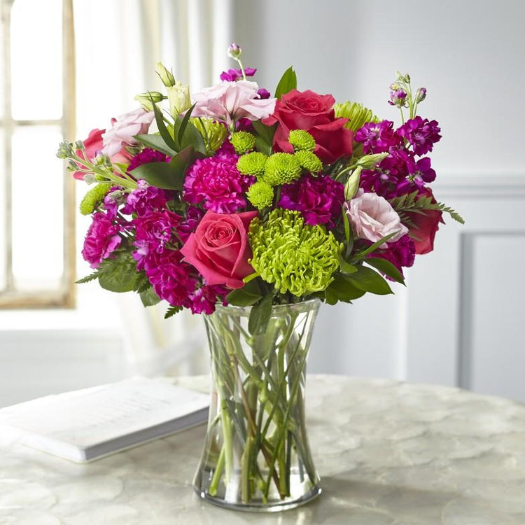 hot pink, fuchsia, and green blooms of f roses, lisianthus, stock and Fuji mums are crafted in a clear vase